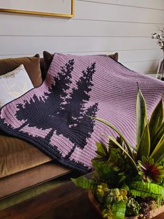 a crocheted blanket on a couch next to a potted plant