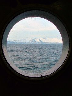 the view from inside a porthole looking out to sea with mountains in the distance