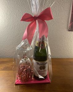 a bottle of champagne in a gift bag with a pink bow on the top, and a glass ornament next to it