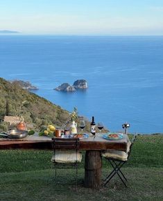 the table is set with food and wine overlooking the water's edge in front of an island