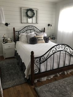 a bedroom with white walls and wood flooring has a black iron bed frame that is topped with pillows