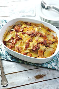 a casserole dish with ham and potatoes in it on a napkin next to silverware