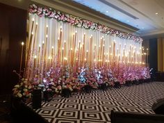 a room filled with lots of flowers and candles in front of a large curtain covered wall