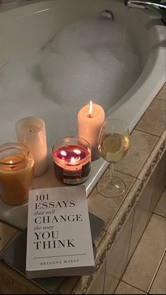 an open book sitting on top of a bath tub next to two glasses of wine