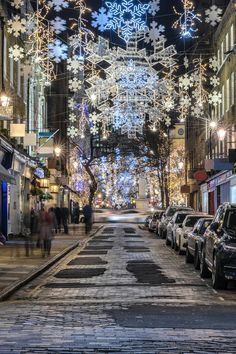 cars parked on the side of a street covered in snowflakes and christmas lights