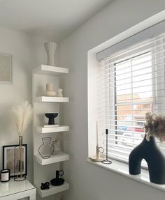 a white room with shelves and vases on the window sill next to it