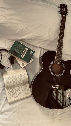 an acoustic guitar, headphones and book on a bed