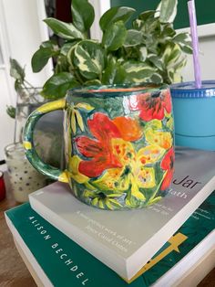 a coffee mug sitting on top of a stack of books next to a potted plant