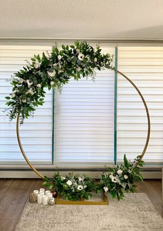 a circular wreath with white flowers and greenery on the floor in front of a window