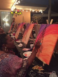 a group of people sitting at a table with paintings on easels in front of them