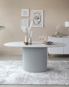 a white table with vases and plants on it in front of a beige wall