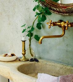 a bathroom sink with a gold faucet next to it and a potted plant in the corner