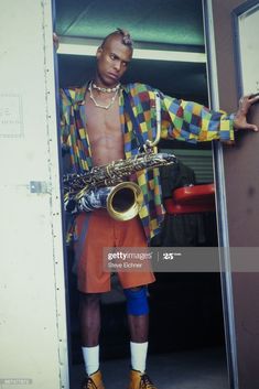 a man standing in an open doorway with a saxophone on his hand and wearing colorful clothing