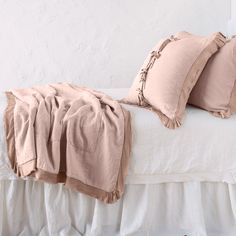 a bed with two pillows on it and a blanket draped over the headboard, in front of a white wall