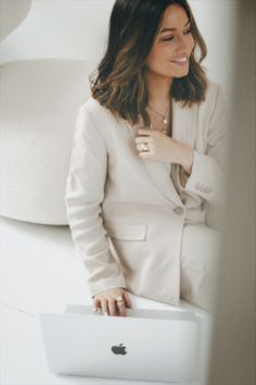 a woman in a white blazer is smiling and holding her lap top up to the side