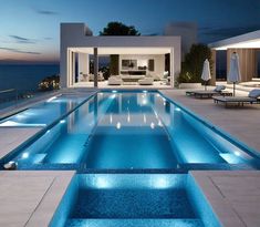 an outdoor swimming pool at night with lounge chairs and umbrellas on the deck overlooking the ocean