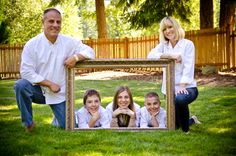 a family posing for a photo in front of a picture frame on the grass with their dog