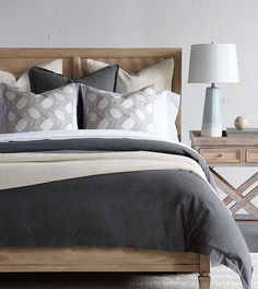 a bed with gray and white pillows on top of it next to a night stand