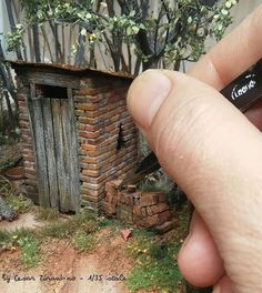 a hand is holding a miniature brick building with a small door and window in it