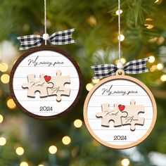 two christmas ornament shaped like puzzle pieces hanging from a tree with lights in the background