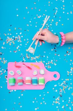 a person holding chopsticks over a pink tray with confetti on it