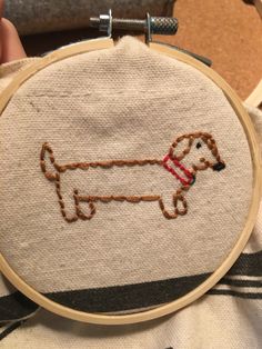 a person holding up a small embroidery project with a dog on it's back