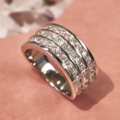 a wedding ring with three rows of diamonds on the inside and outside, sitting on a pink surface