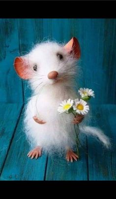 a stuffed rat with flowers in it's paws on a blue wooden table next to some wood planks