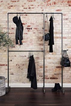 a brick wall with clothes hanging on hooks and purses in front of the coat rack