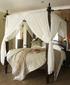 a four poster bed with white drapes on it's headboard and foot board