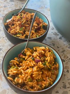 two bowls filled with pasta and vegetables on top of a marble counter next to a blue pot