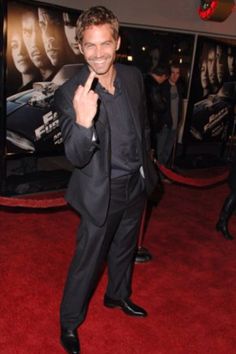 a man in a suit and tie giving the peace sign on a red carpeted area