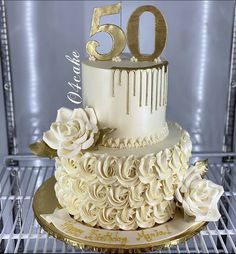 a 50th birthday cake decorated with white flowers and gold lettering on a metal rack in a refrigerator