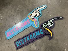 two stickers that say restrooms, rest rooms and pointing fingers at each other