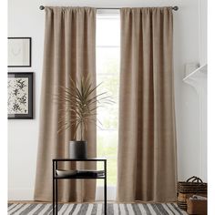 a living room with a large window covered in curtains and a potted plant next to it