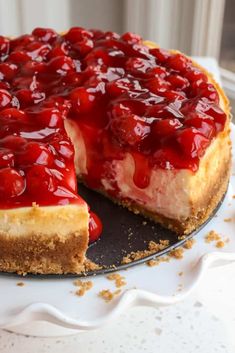 a cheesecake covered in cherries on top of a cake plate with one slice missing