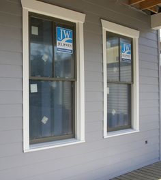 two windows on the side of a gray house with blue and white signs above them