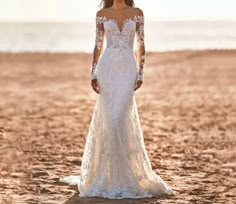 a woman standing on top of a sandy beach next to the ocean wearing a wedding dress