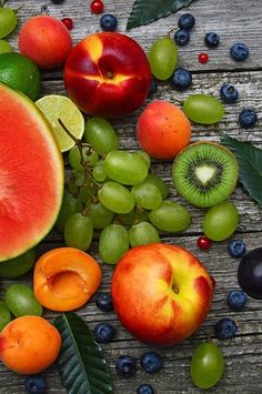 an assortment of fresh fruit on a wooden table with leaves and berries around it, including kiwis