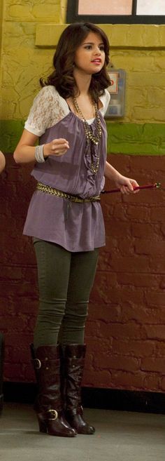 a woman standing in front of a brick wall holding a wand and pointing at something