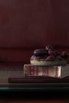 a bowl of plums sitting on top of two books