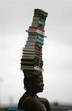 a woman is carrying a stack of books on her head