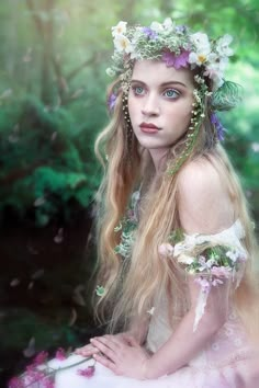 a woman with long hair and flowers in her hair sitting on the ground next to trees