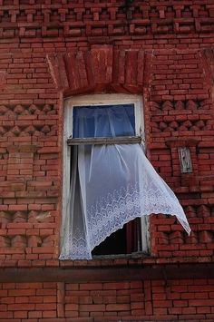 an open window on the side of a brick building with a white curtain hanging from it