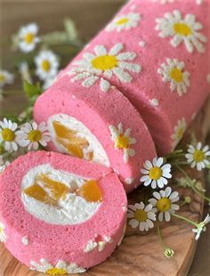 a pink cake with white flowers on it is cut in half and sits on a cutting board