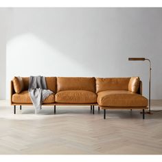 a brown leather couch sitting on top of a hard wood floor next to a lamp