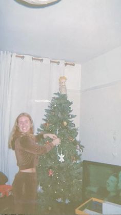 a woman standing next to a christmas tree in front of a clock on the wall