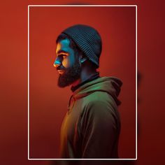 a man with a beard wearing a beanie looks off into the distance while standing in front of a red background