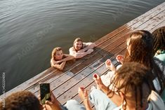 a group of people sitting on top of a wooden pier next to the water taking pictures