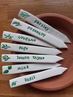 five white spoons with green writing on them sitting in a clay bowl next to a wooden table